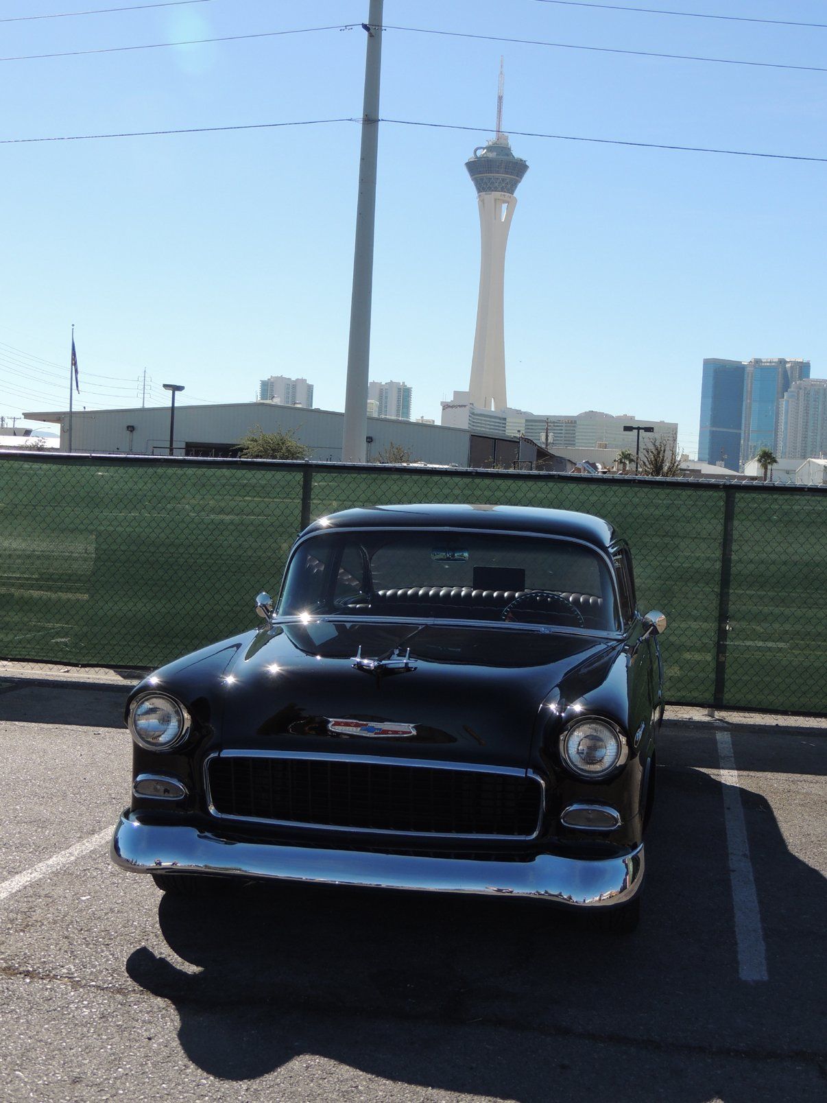 A black car is parked in a parking lot in front of a fence