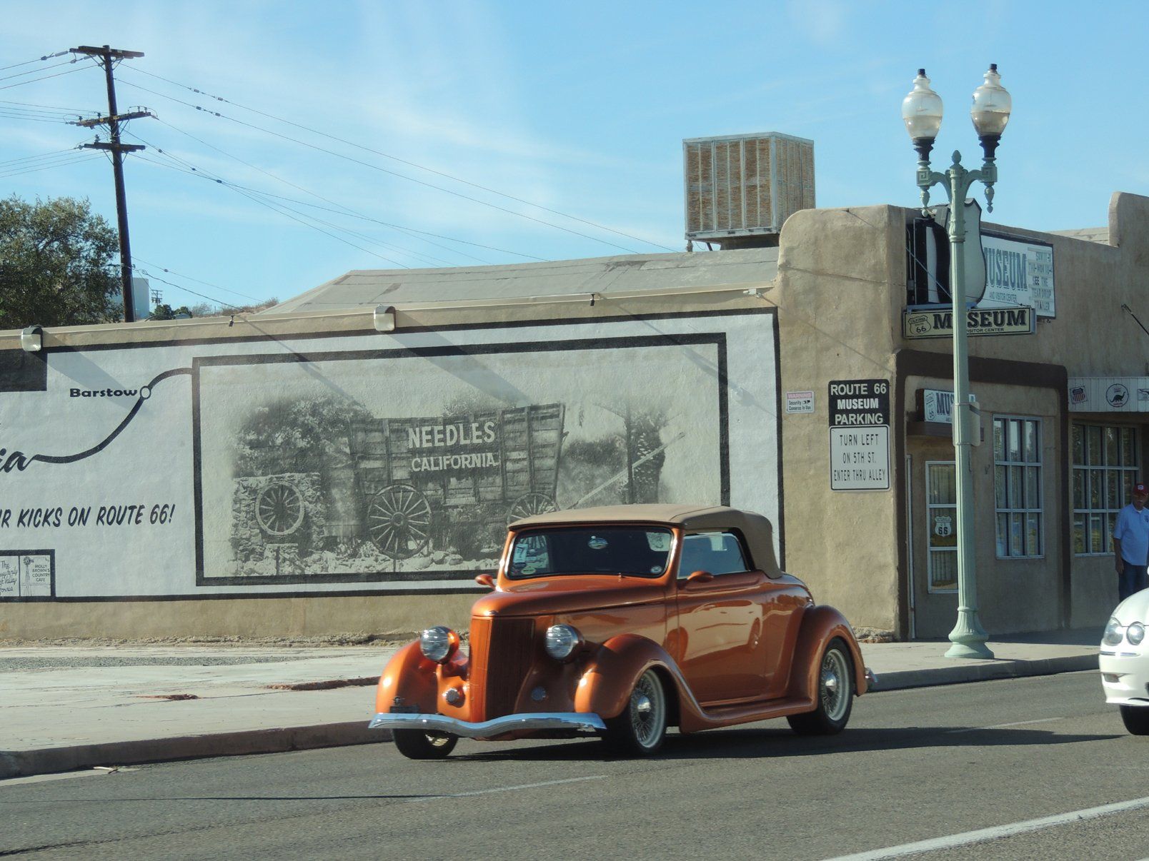 An old car is parked in front of a building that says needles repair