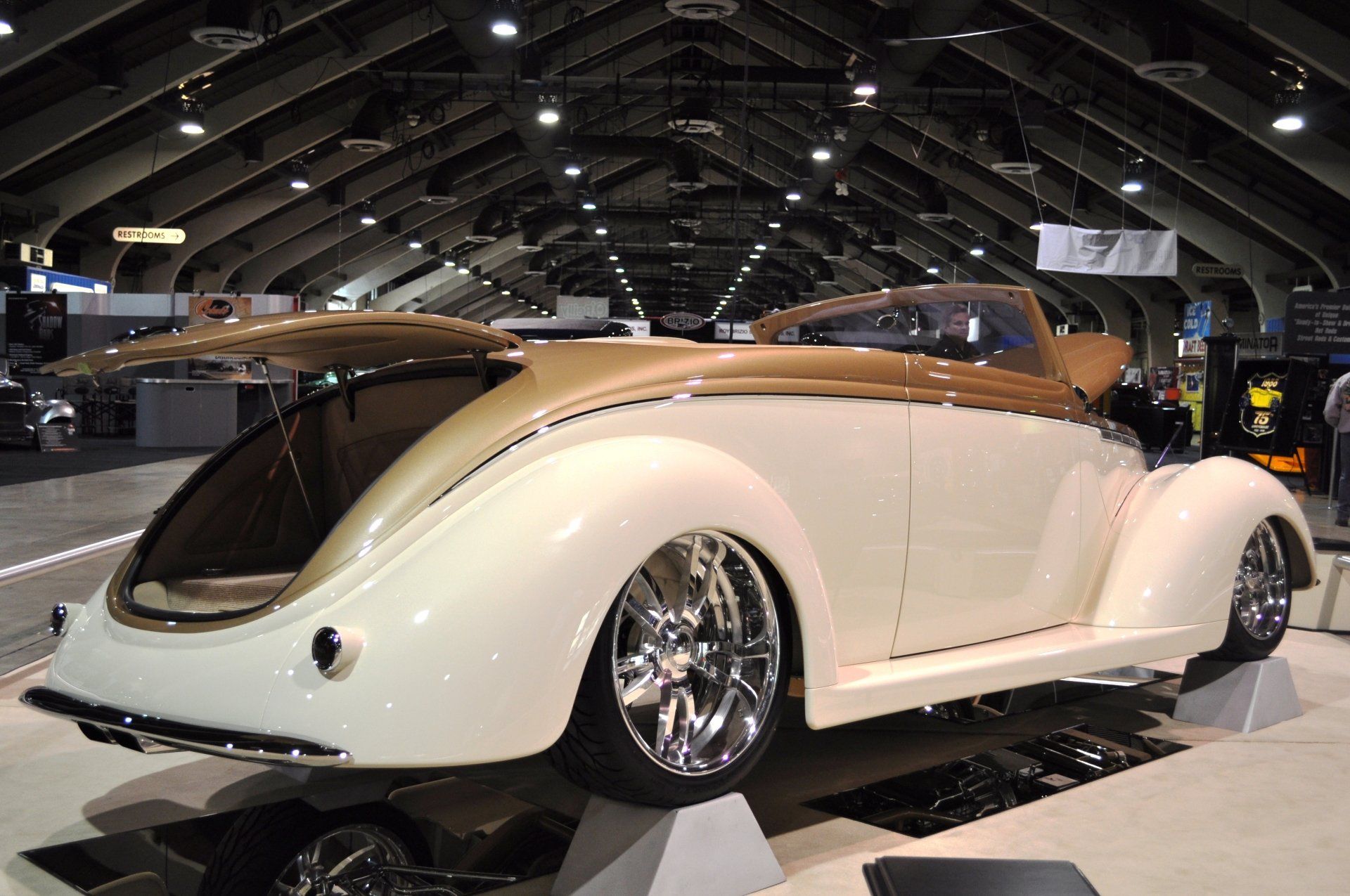A white car with the trunk open is on display at a car show