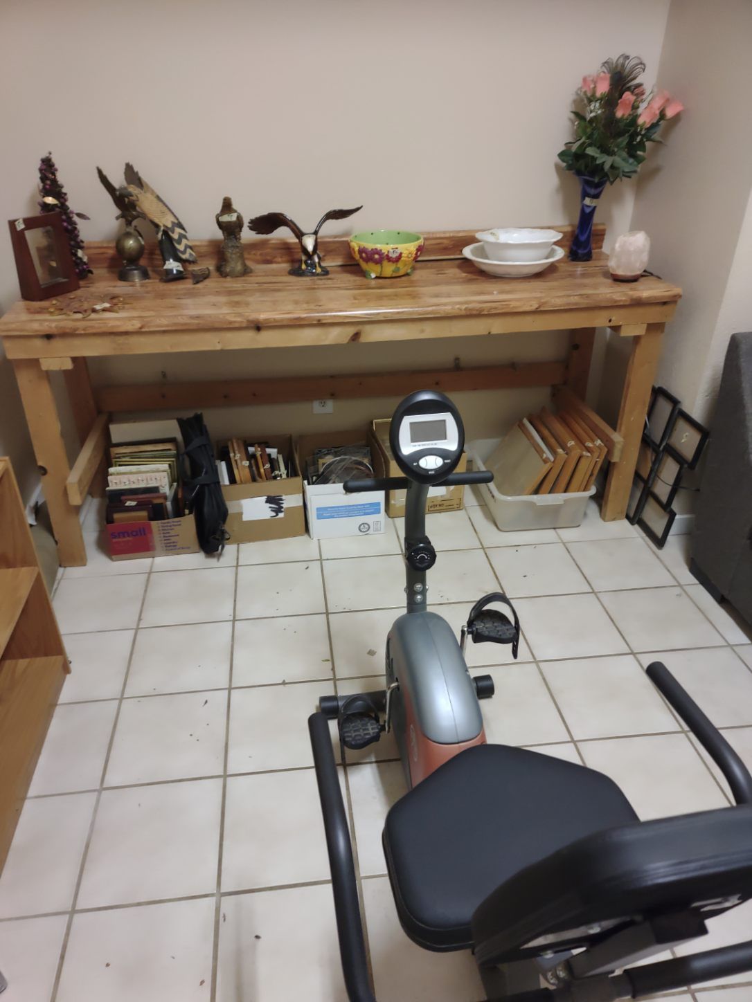 Stationary bike in front of a wooden table with various items, set in a room with tiled floor.