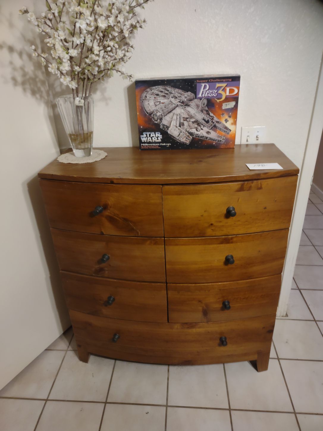 Wooden dresser with six drawers, vase of flowers, and a Star Wars puzzle on top.