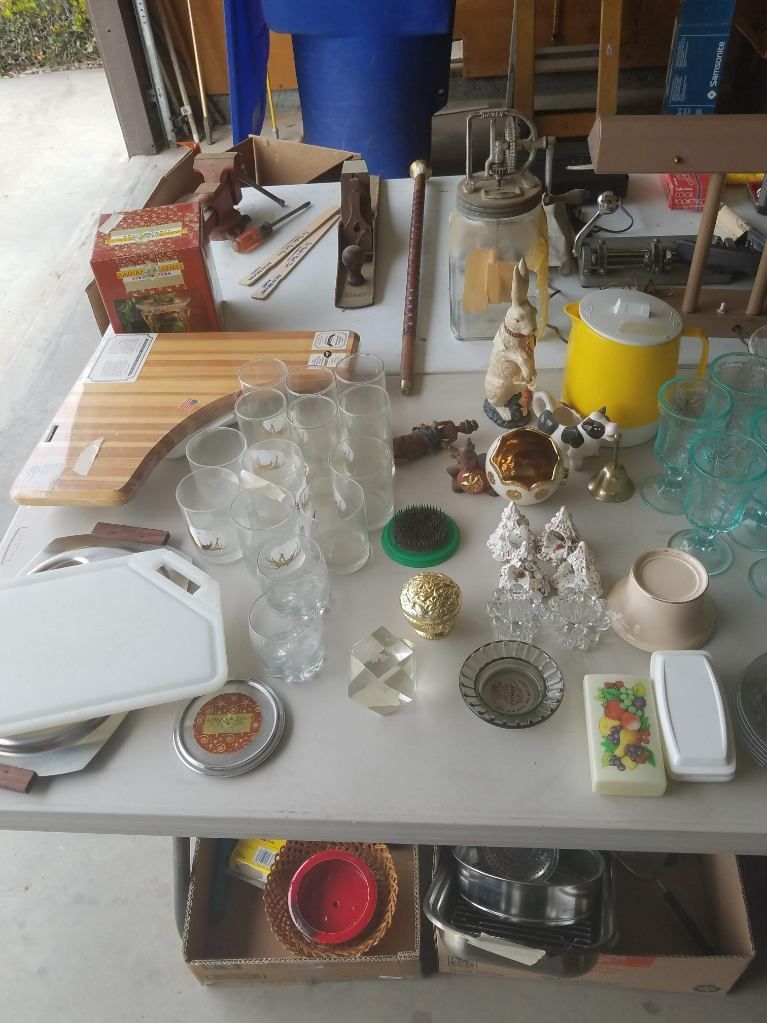 Table with miscellaneous items for sale, including glassware, decor, and kitchenware.