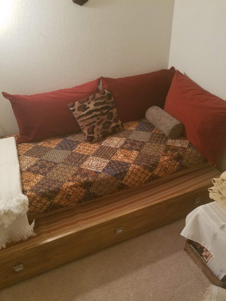 Daybed with red and animal print cushions, wooden base, and a white blanket.