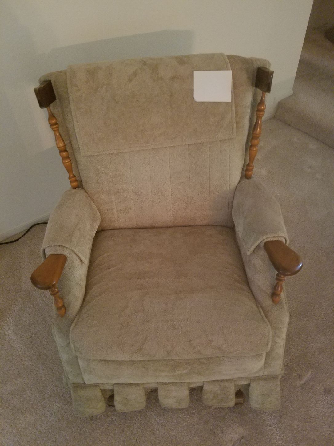 Beige upholstered armchair with wood accents, against a light-colored wall.