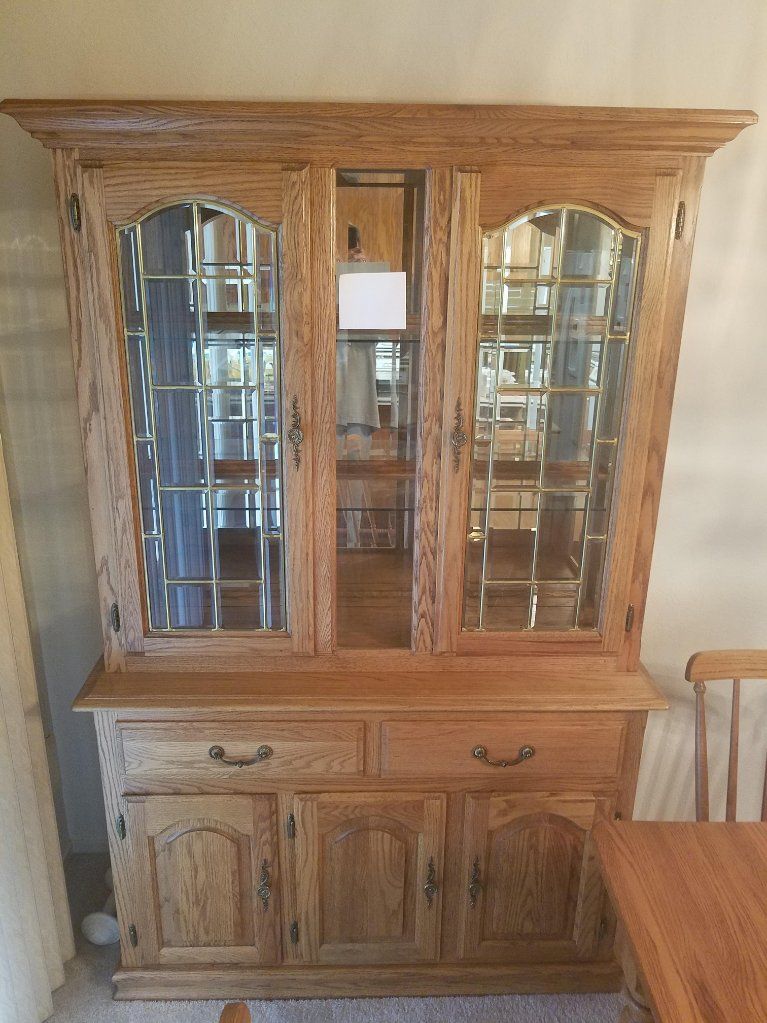 Wooden hutch with glass doors, drawers, and cabinet doors, in a room with light-colored walls and a dining table.