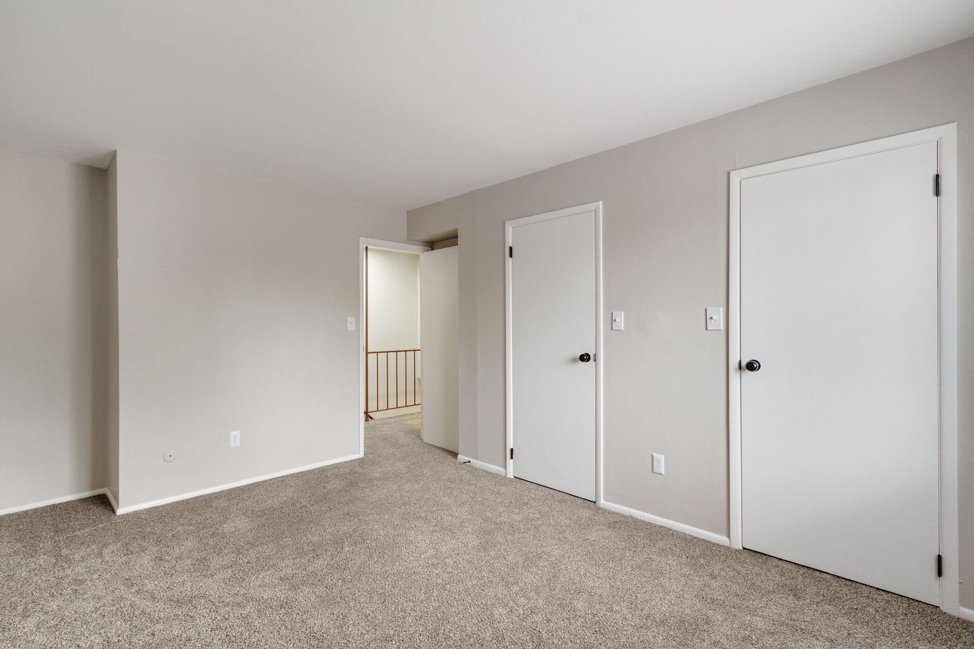 Empty bedroom with beige walls, carpet, and two white doors.