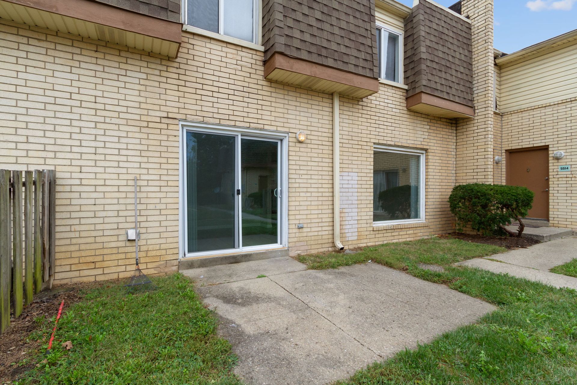 Brick townhouse exterior with sliding glass door, concrete patio, and small grassy area.