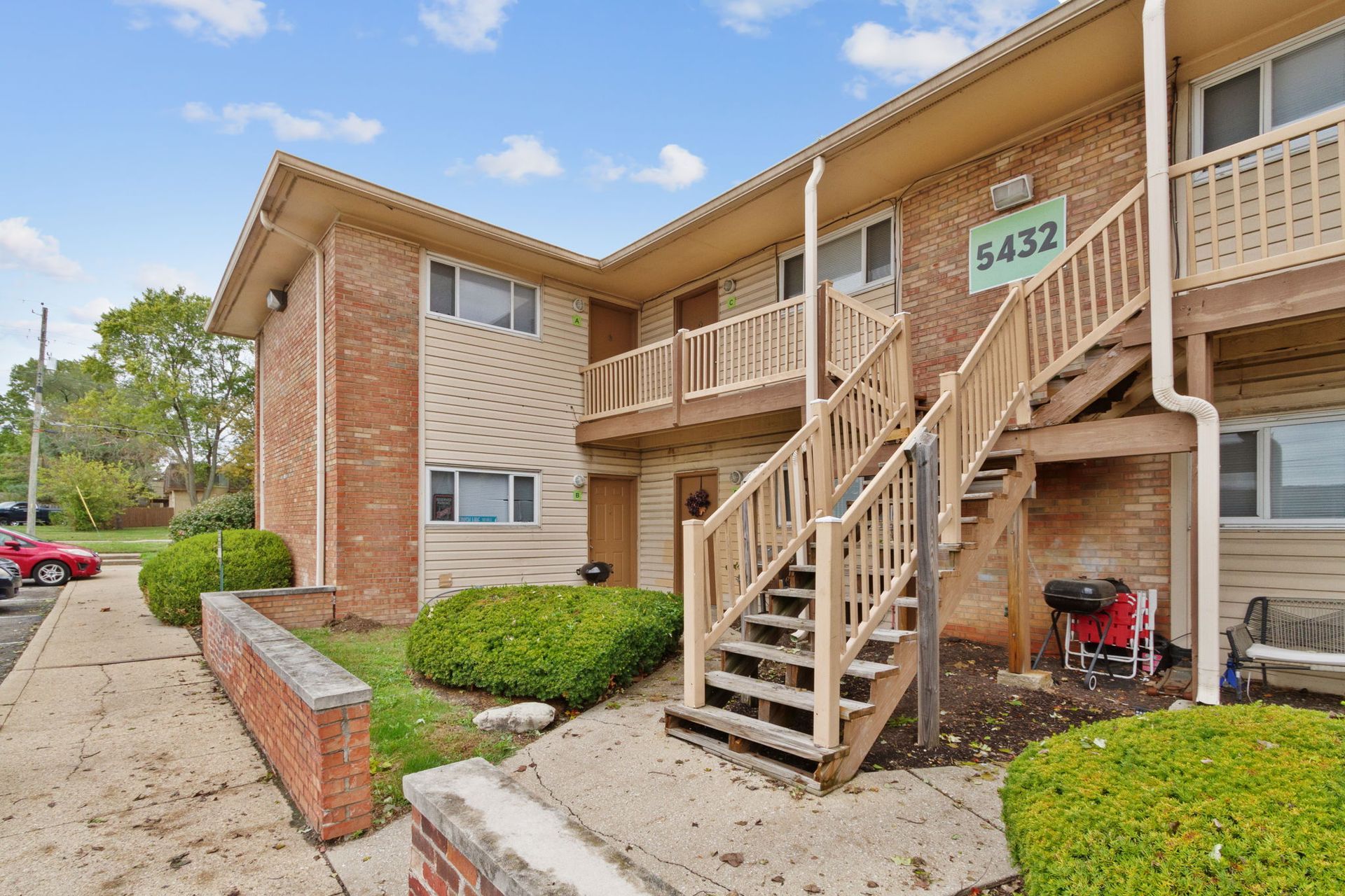 Two-story apartment building with stairs to upper units. Address 5432. Landscaping and parked cars visible.