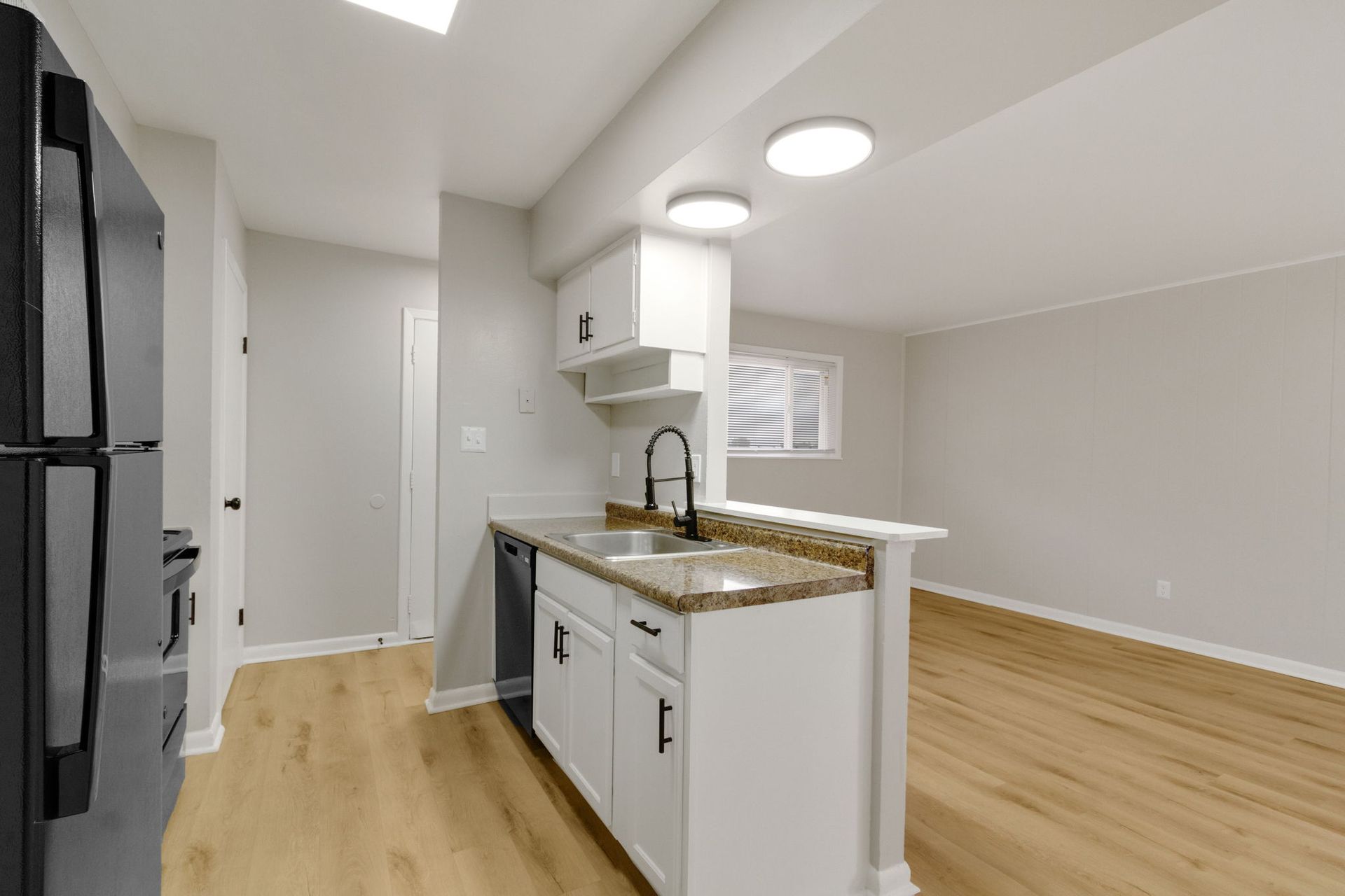 Kitchen with white cabinets, black appliances, and light wood flooring. Open to a living area.