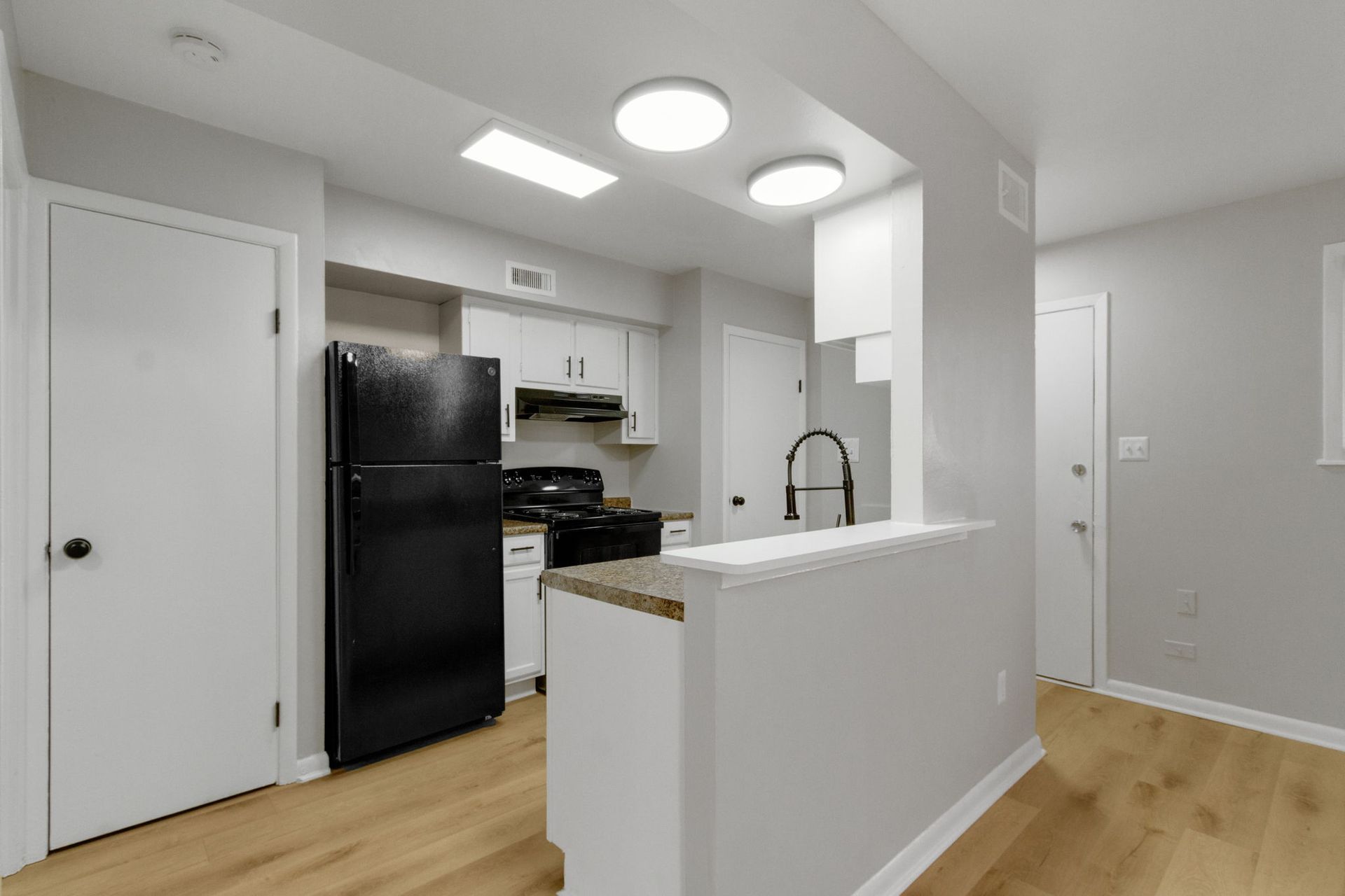 A small kitchen with black appliances, white cabinets, and light-colored wood-look flooring.