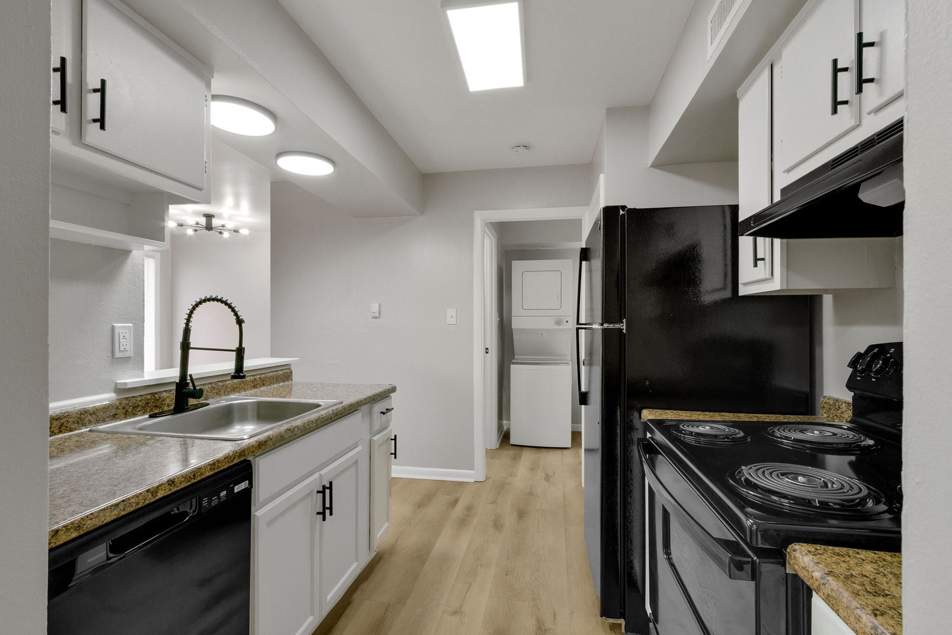Kitchen with white cabinets, black appliances, and a view of the laundry area.