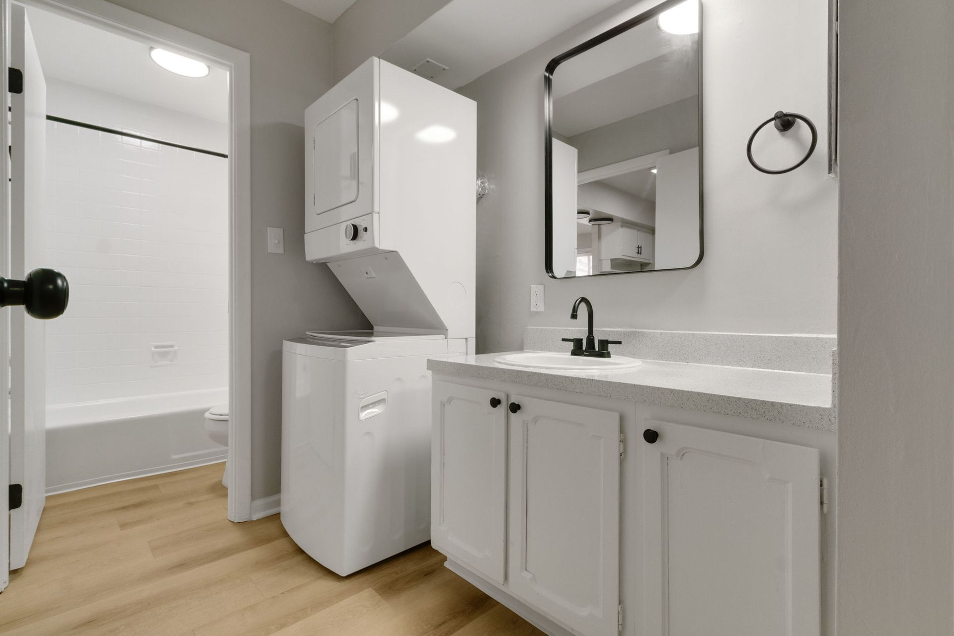 A small, modern bathroom with a stacked washer and dryer, white vanity, and an open doorway.