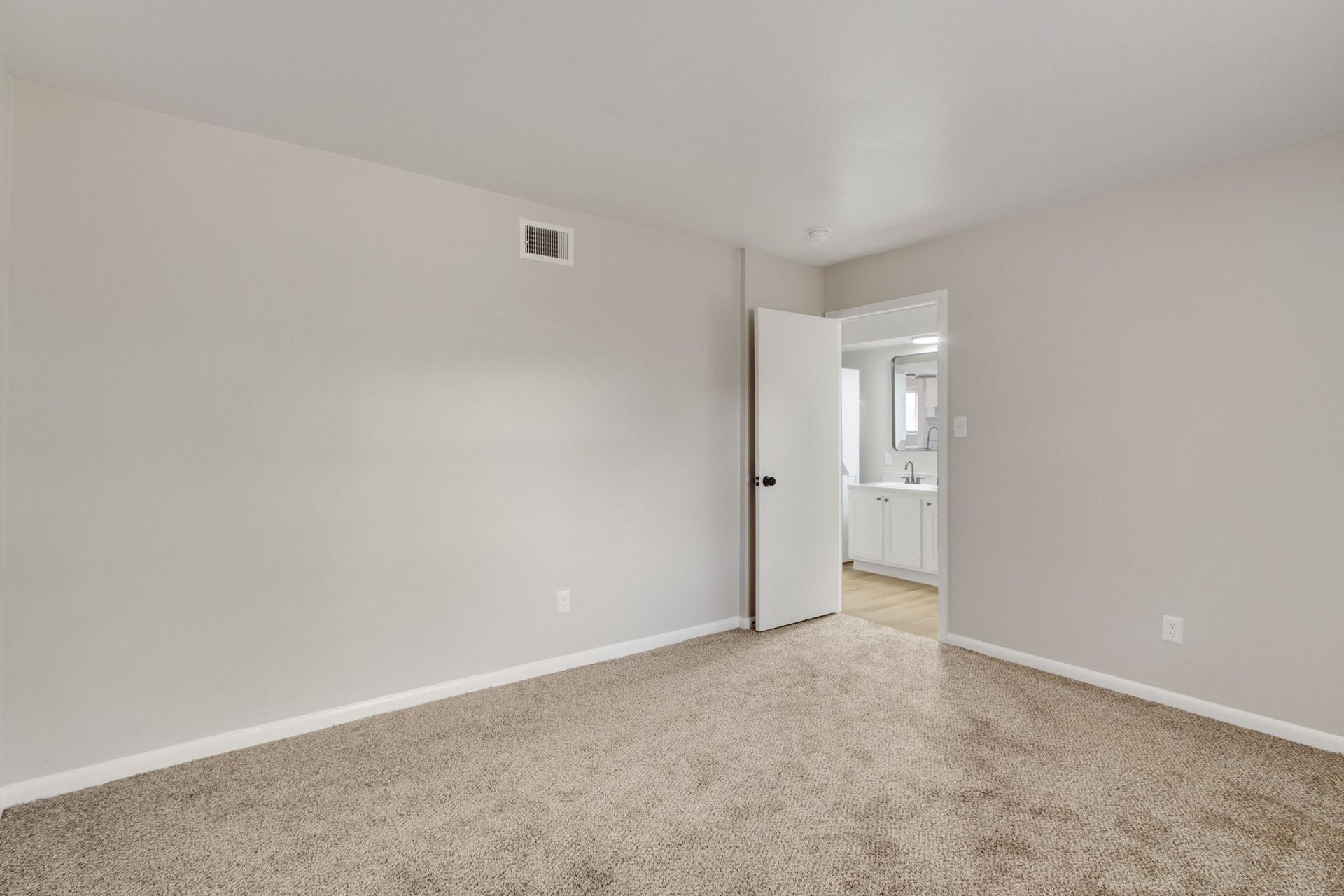 Empty bedroom with beige carpet, gray walls, and doorway to a bathroom.