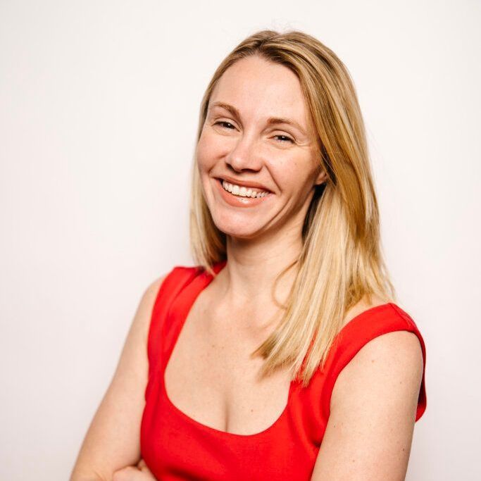 A woman in a red top is smiling with her arms crossed