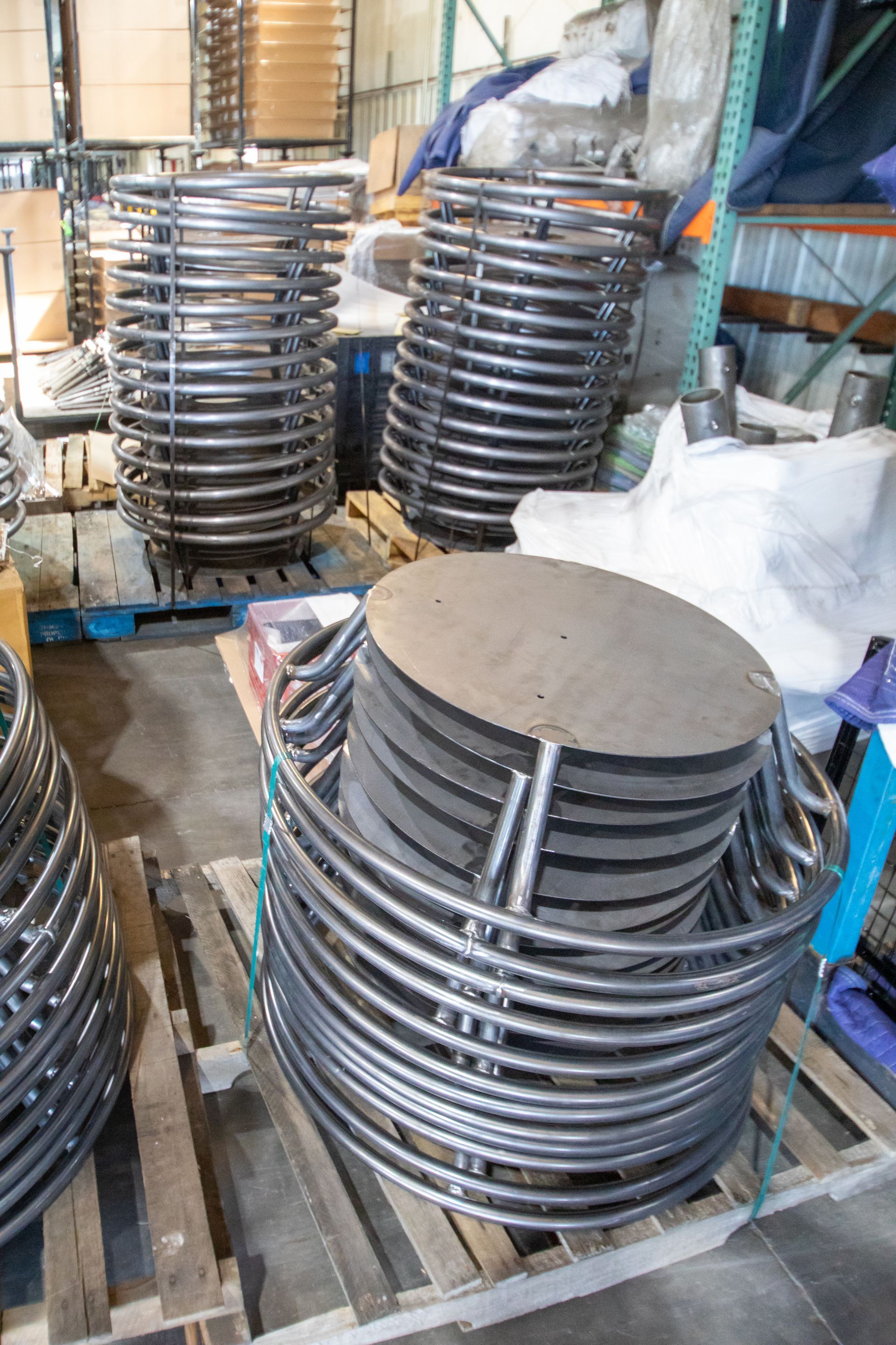 Metal coils and circular platforms stacked on pallets in a warehouse.
