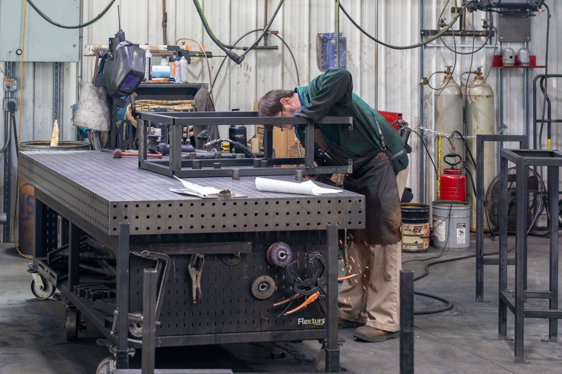 Man welds metal frame at a workshop. He is bent over a large black table.