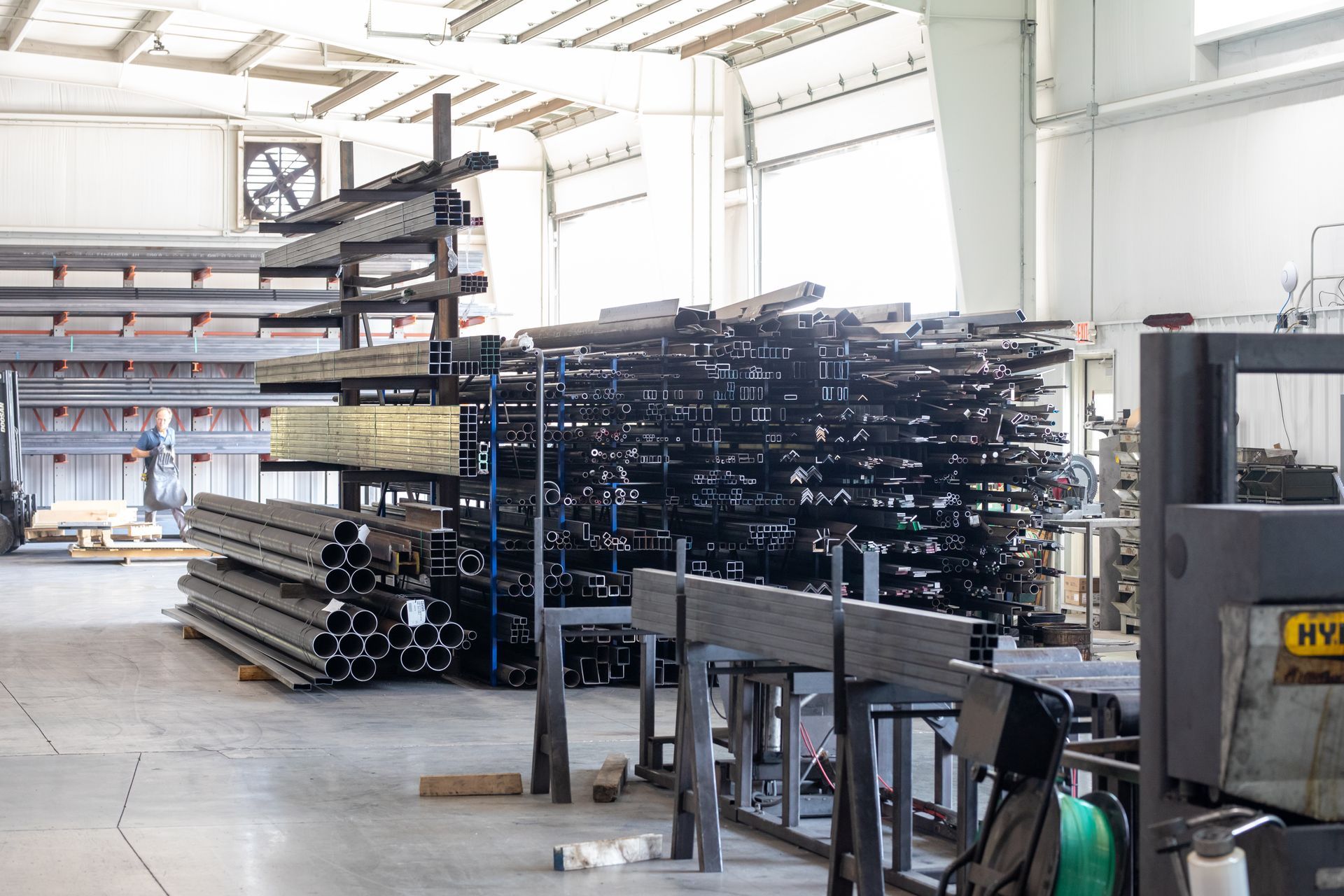 Steel beams and pipes stacked on industrial shelving in a warehouse setting.