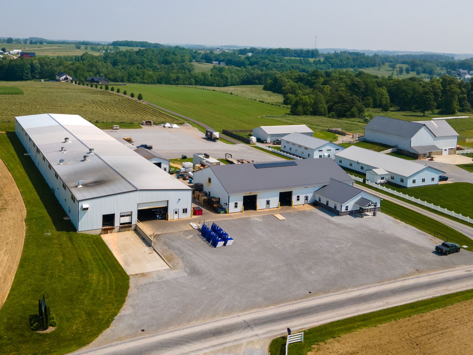 Aerial view of industrial buildings on a rural property with a paved lot and green fields in the background.