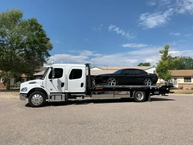 A tow truck is carrying a black car on the back of it.
