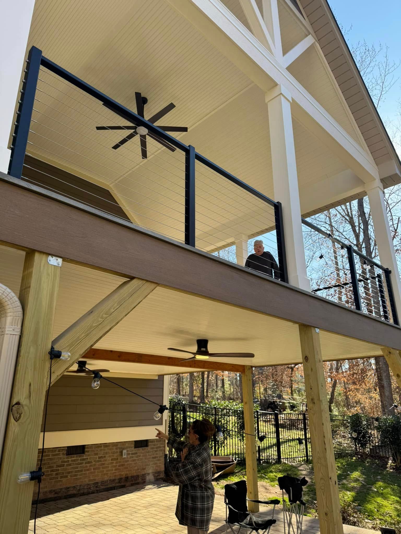 A man is standing on a balcony of a house with a ceiling fan.