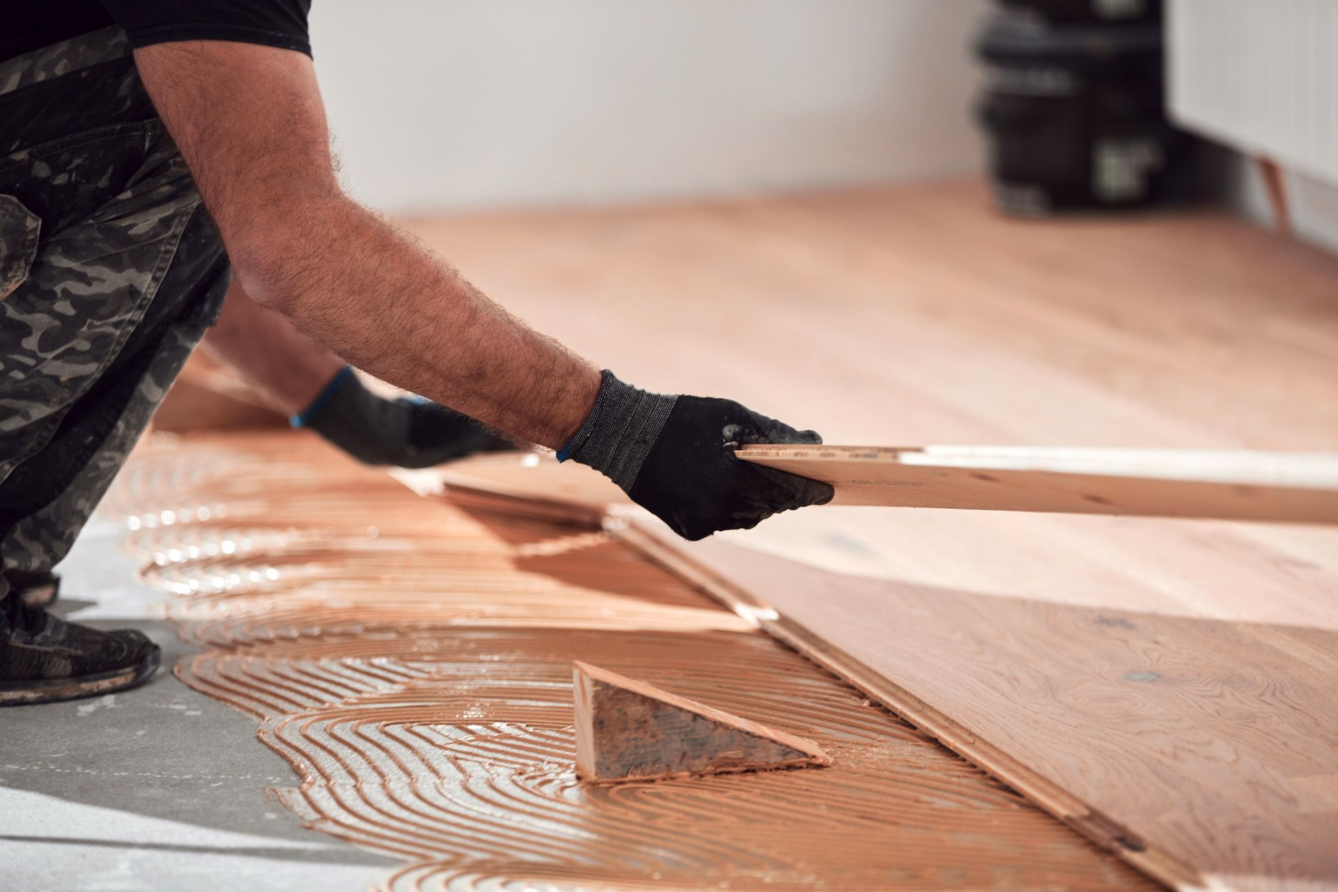 Person installing wooden floorboards, using glue.
