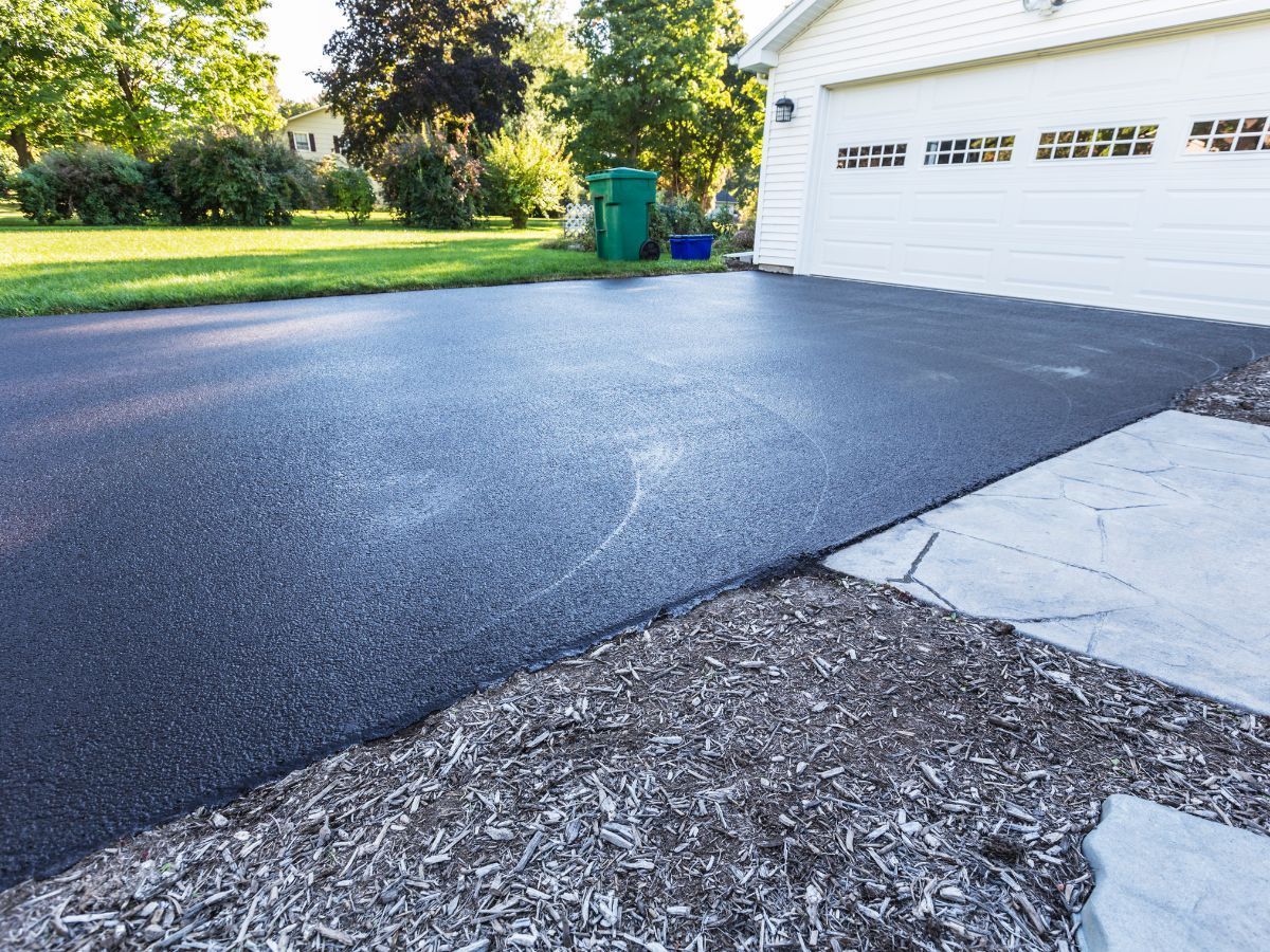 A black asphalt driveway with a white garage in the background.