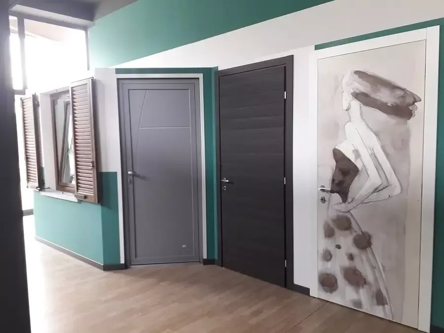 Un corridoio con pavimento in legno chiaro, una parete con dettagli verdi, una porta grigia, una porta in legno scuro e una porta decorata con uno schizzo.