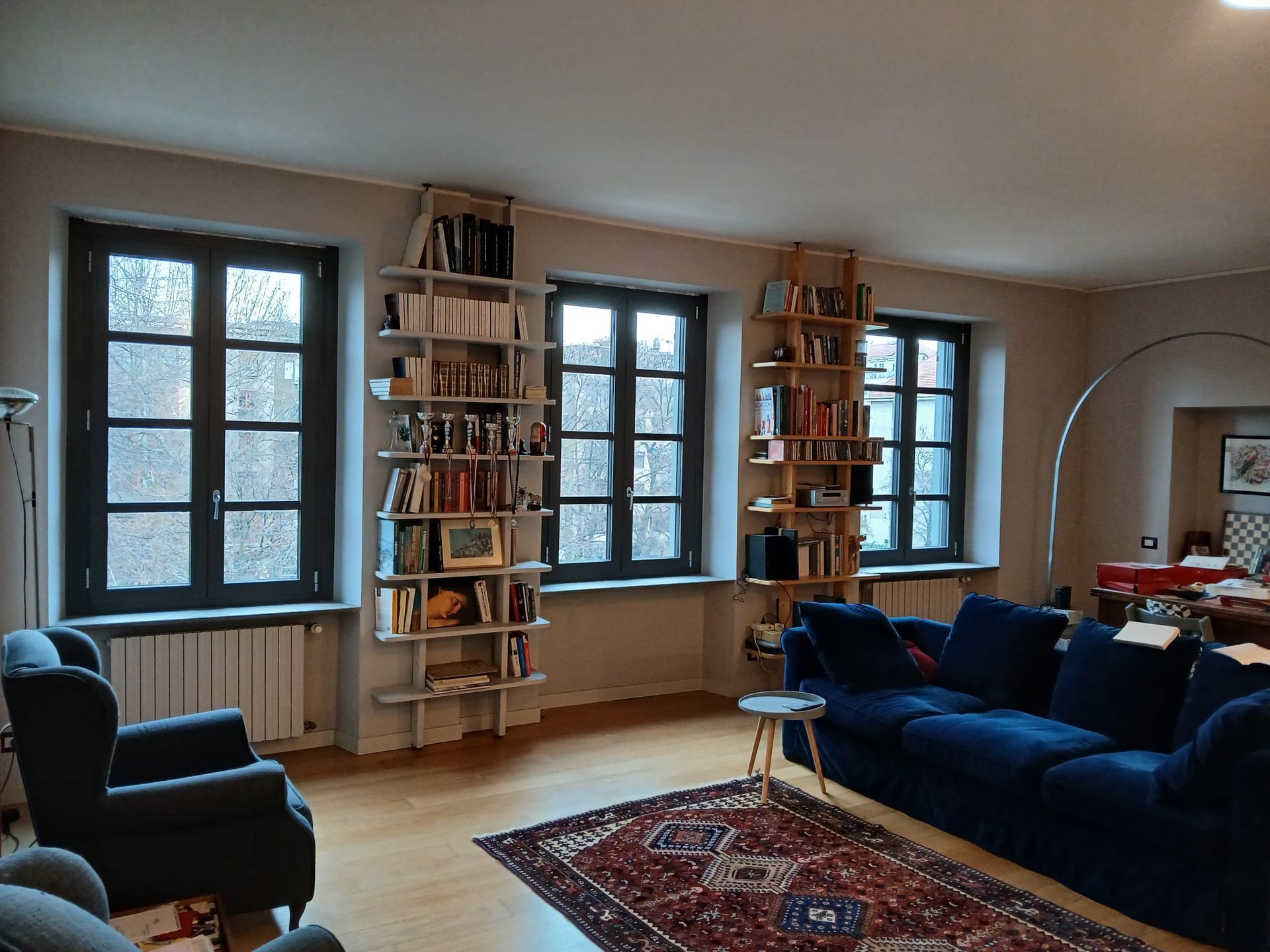 Una stanza con pareti color verde acqua, una finestra con persiane marroni, una porta grigio chiaro e un'altra porta marrone scuro su un pavimento in legno.