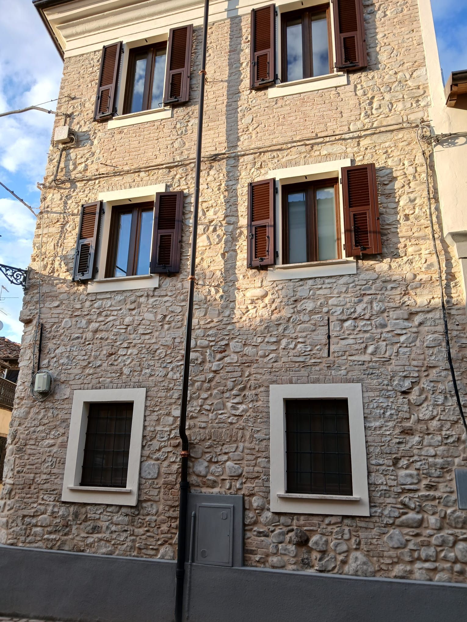 Una finestra con persiane aperte e una piccola pianta in vaso sul davanzale, incastonata in una parete di stucco rosa chiaro sotto una sporgenza del tetto.