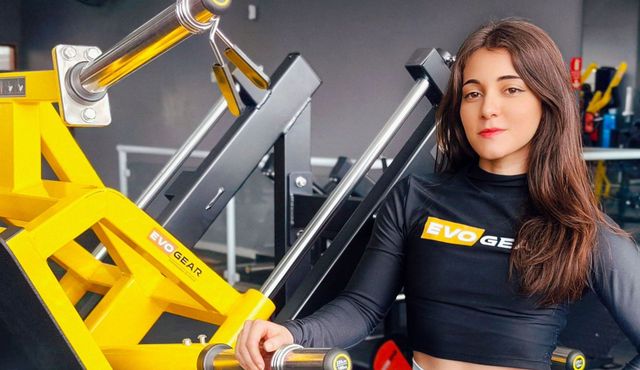 A woman is standing next to a yellow machine from EvoGear in a gym.