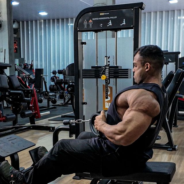 A man is sitting on a machine in a gym.