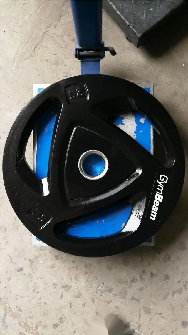 Una placa de pesas de viga de gimnasio descansa sobre un piso de concreto