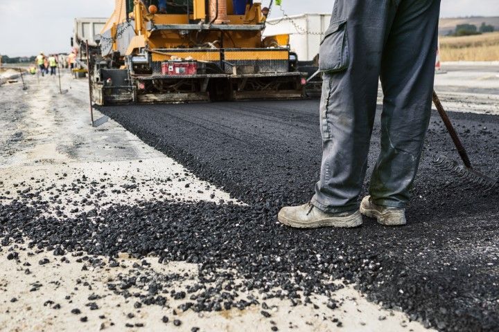 Road worker stands by asphalt paving machine laying down fresh asphalt.