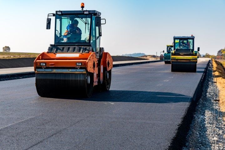Road rollers compacting fresh asphalt on a sunny day.