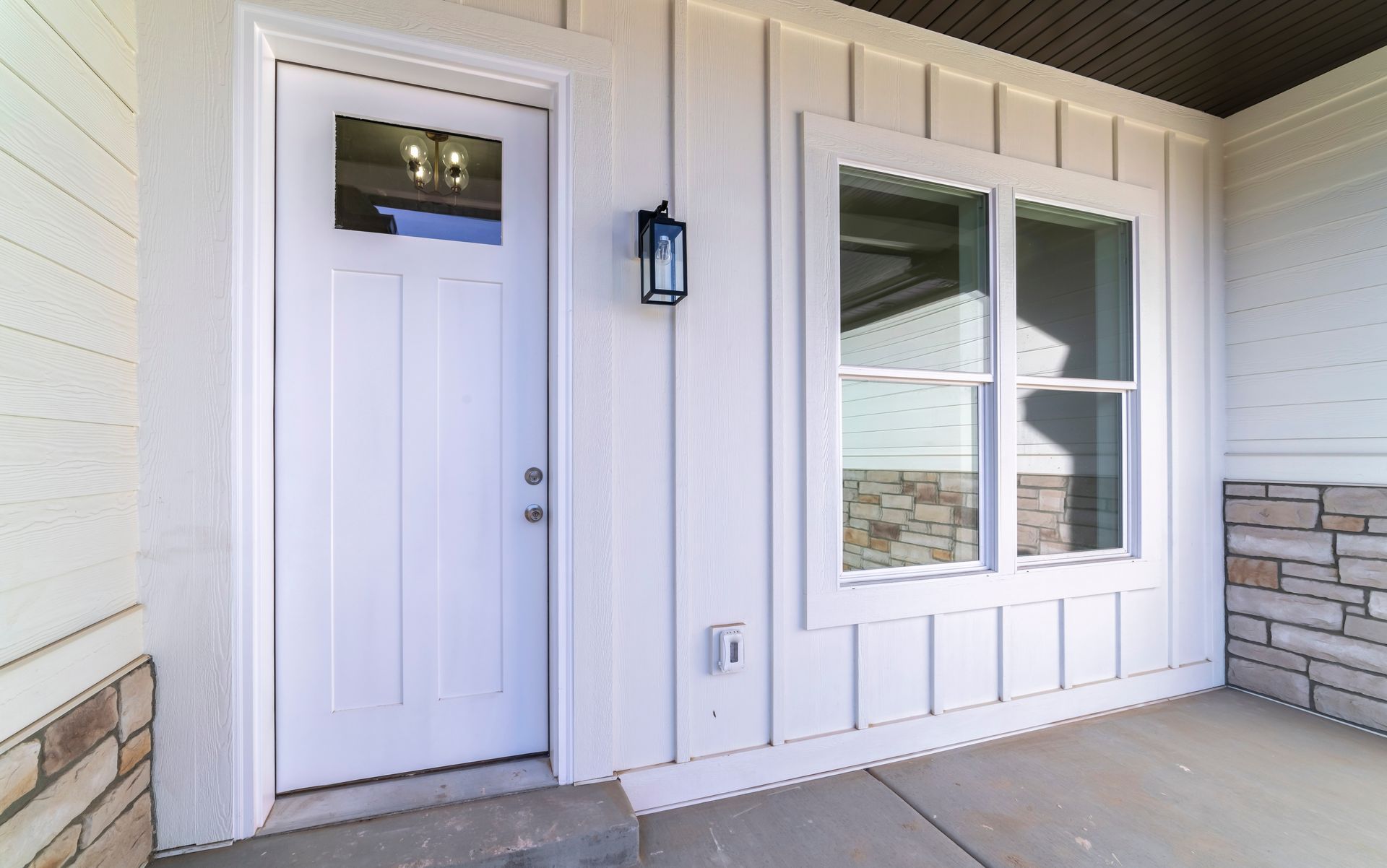 White front door with glass panel, beside a window on a light-colored house with stone accents.