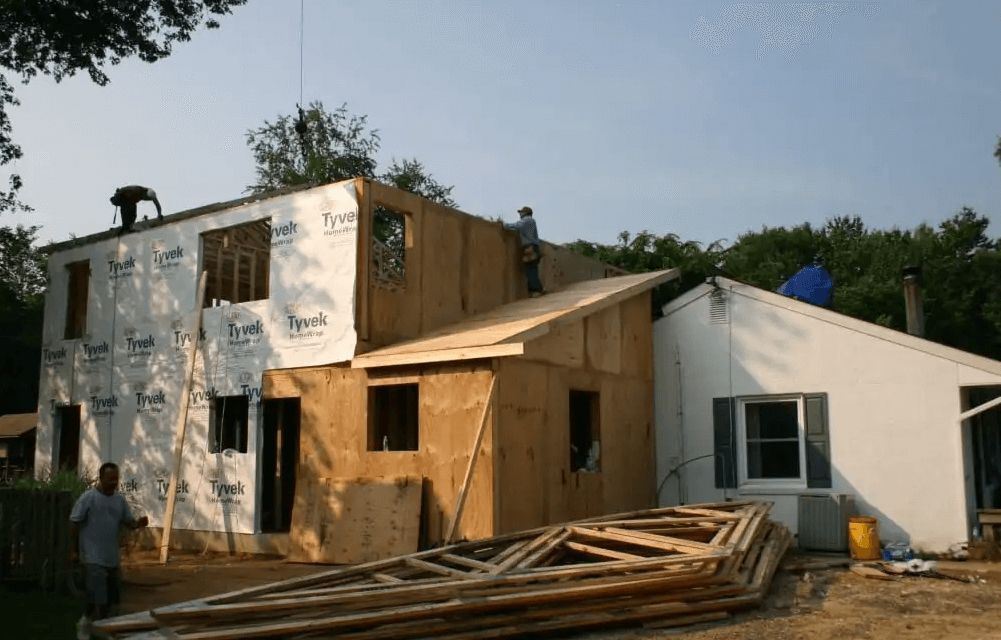 A house is being remodeled with a stack of wood in front of it.