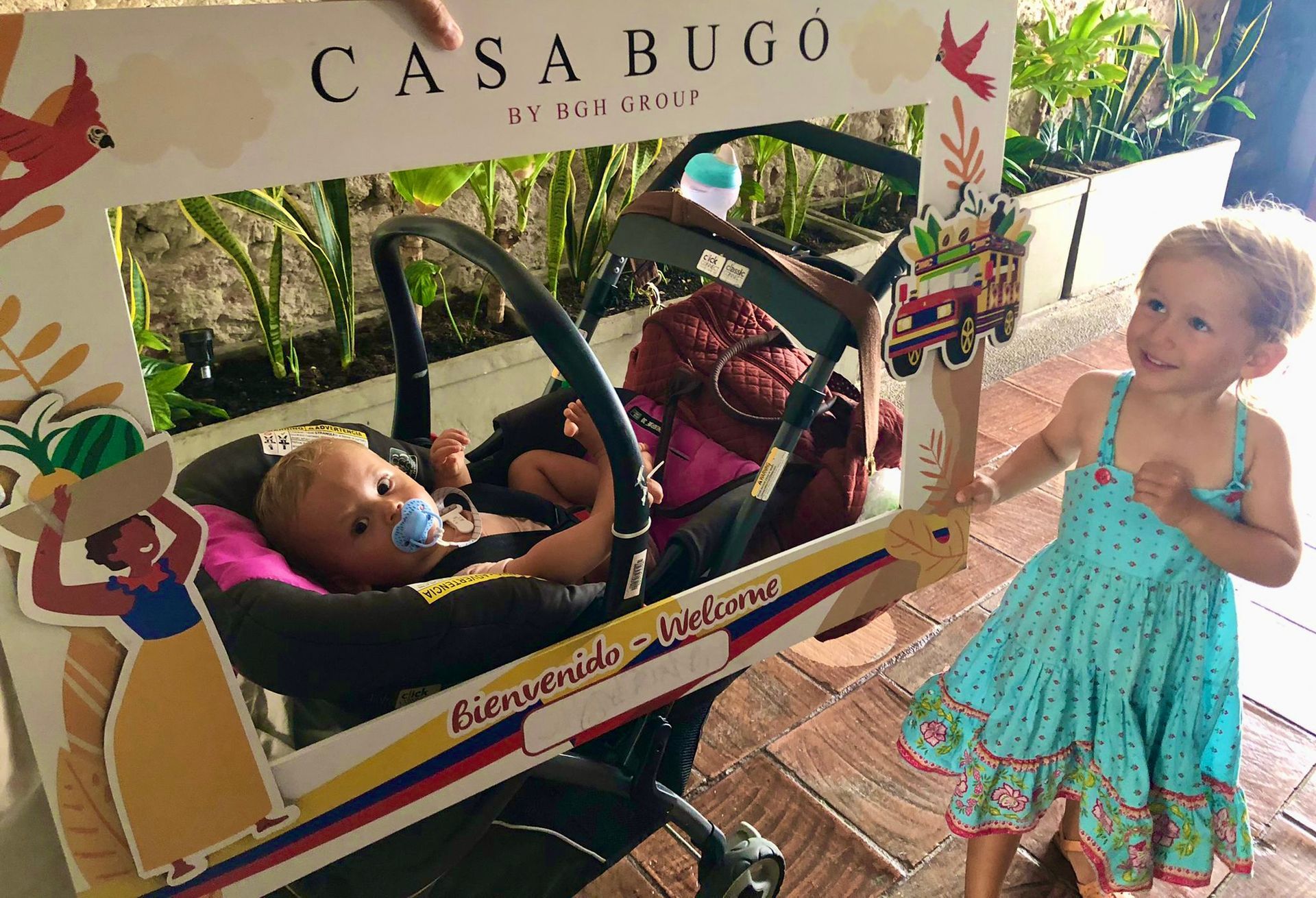 Two little girls are standing next to a baby in a stroller