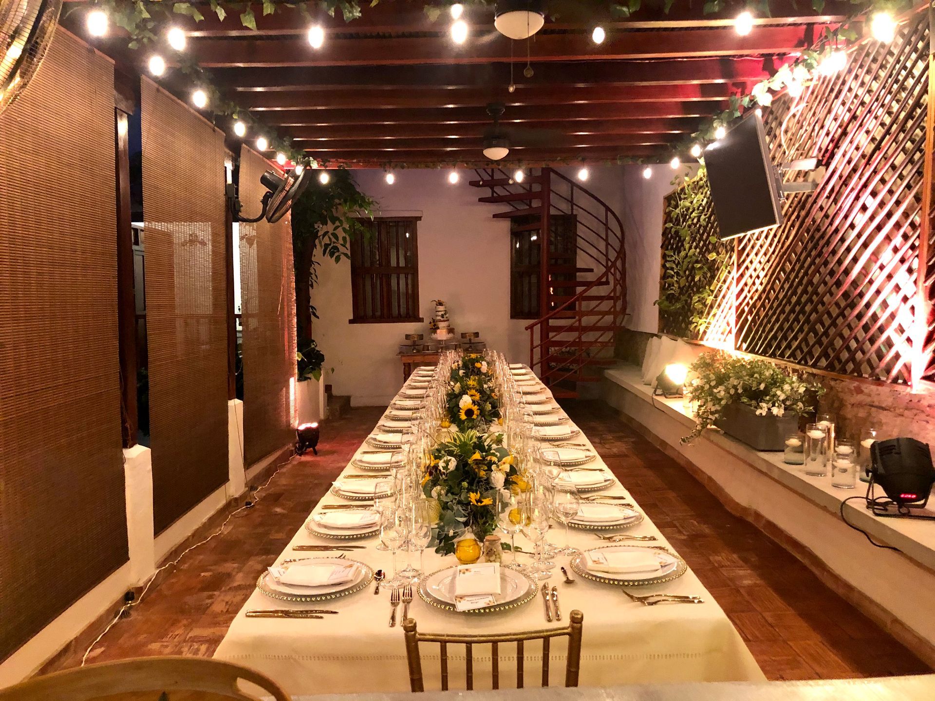 A long table with plates and glasses in a room with a spiral staircase.
