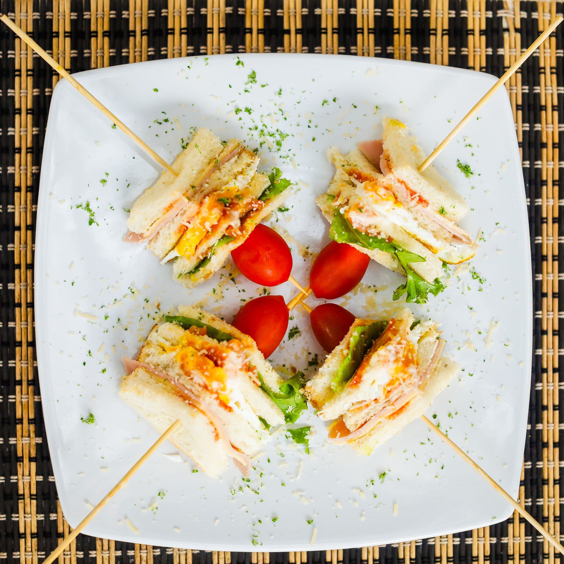 A white plate topped with sandwiches and tomatoes on sticks