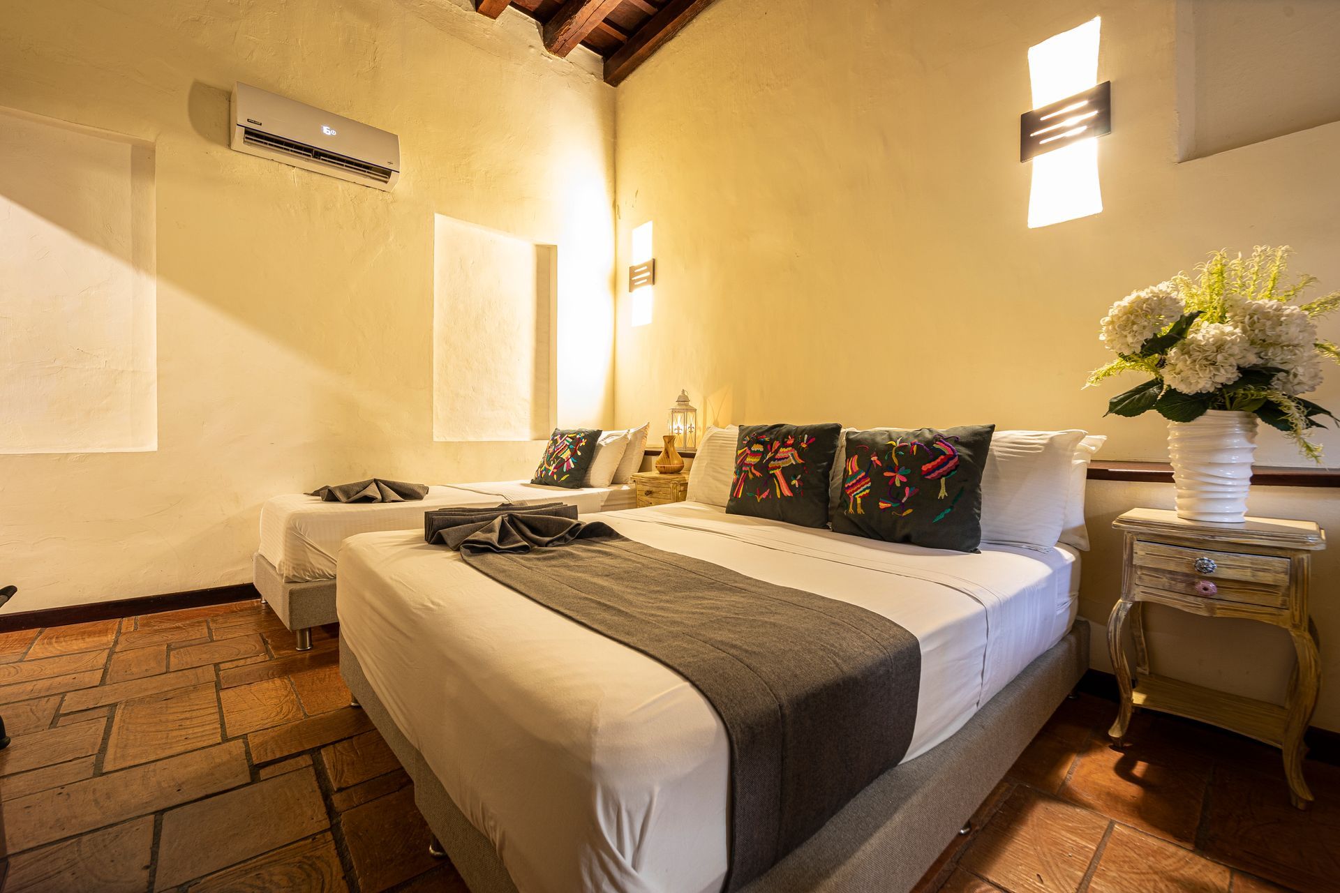 A hotel room with two beds and a vase of flowers on the nightstand.