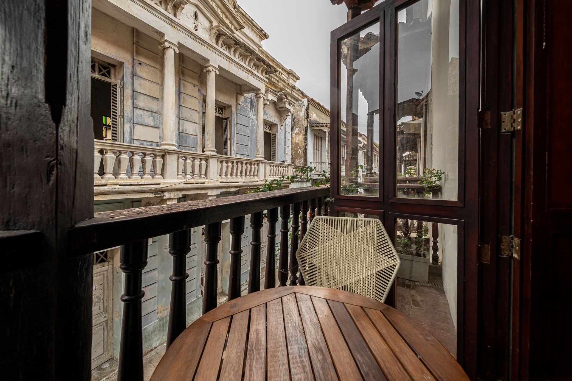 A balcony with a wooden table and chairs and a building in the background.