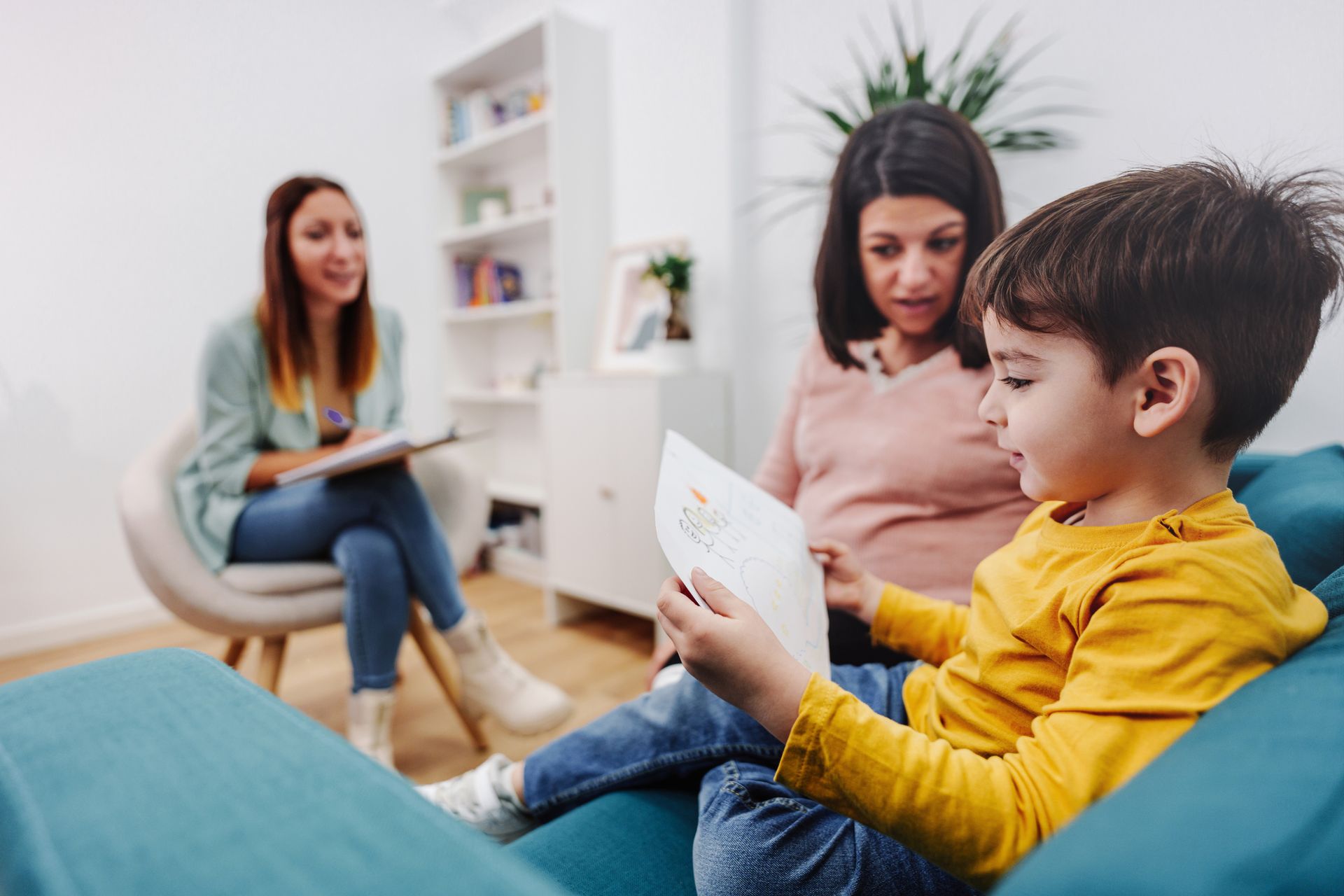 A little boy is sitting on a couch reading a book to his mother.