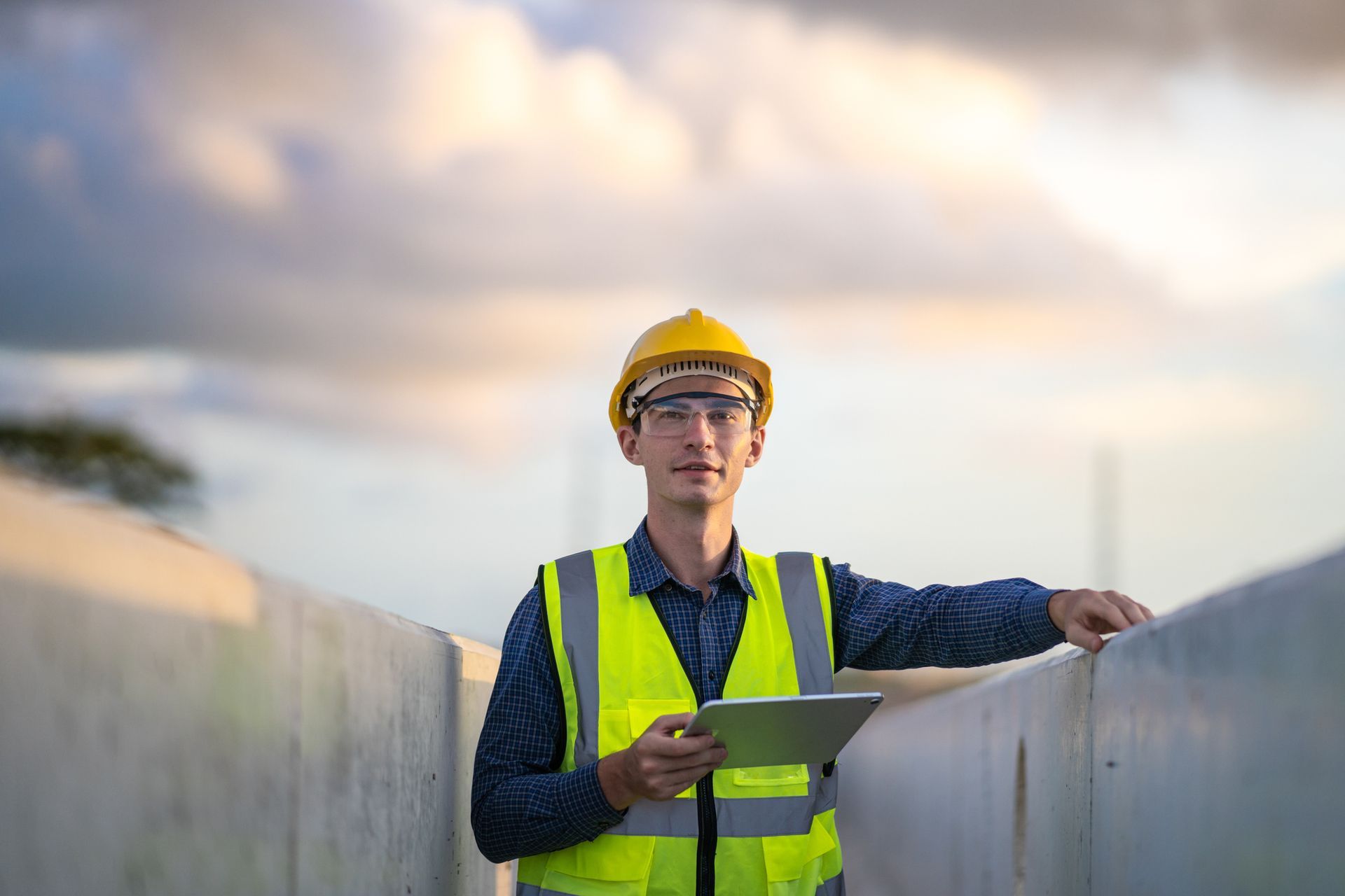 A construction worker is standing next to a wall holding a tablet.