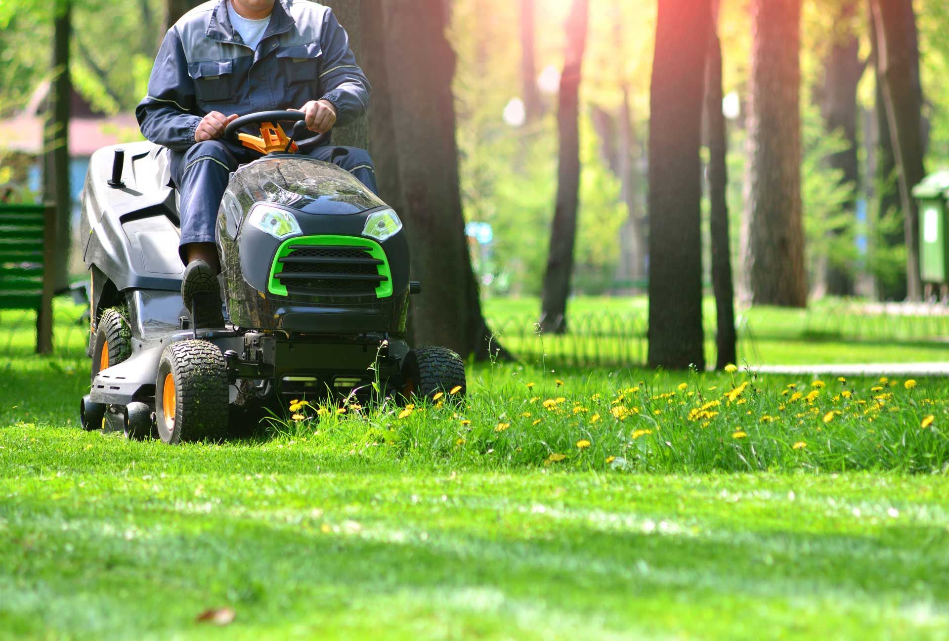 Person mowing grass with a riding lawnmower in a sunny park setting. Person mowing grass with a riding lawnmower in a sunny park setting.