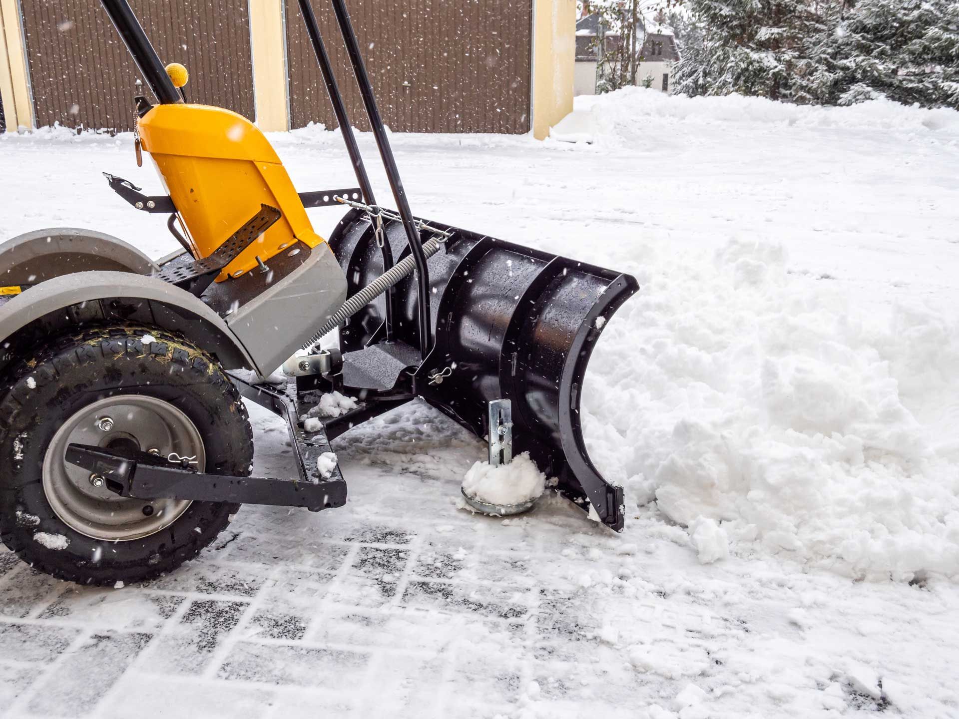 Yellow snow plow clearing snow from a paved driveway.