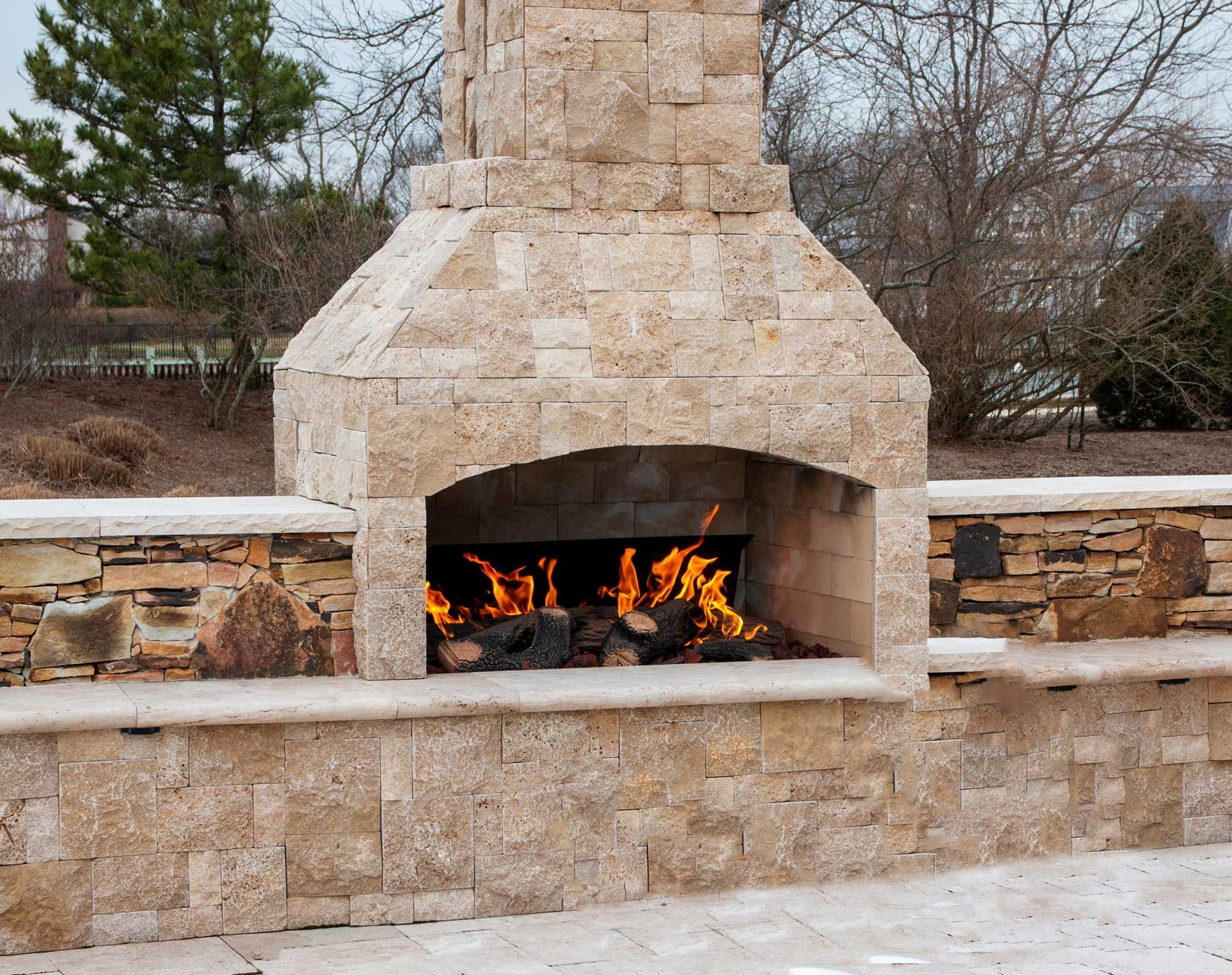 Stone outdoor fireplace with fire burning, set in a stone wall. Stone outdoor fireplace with fire burning, set in a stone wall.