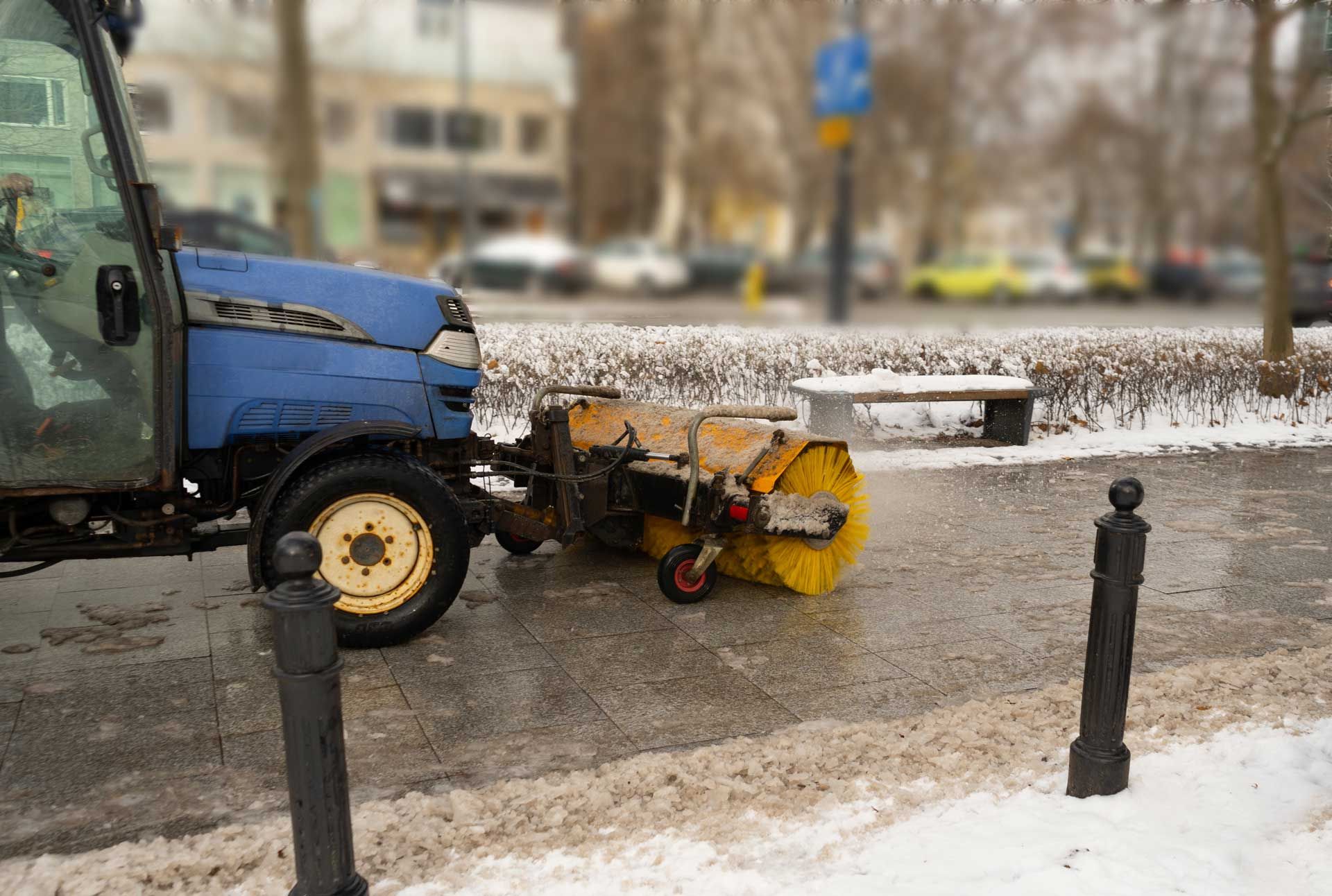 Blue street sweeper clearing snow from a sidewalk.
