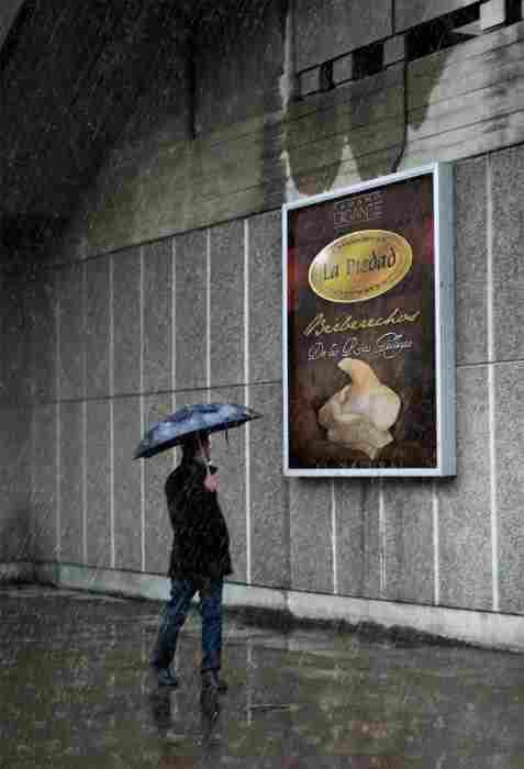 Una persona, protegida por un paraguas, permanece de pie en una acera mojada por la noche, mirando un anuncio brillantemente iluminado en una pared de hormigón.