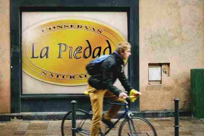Una persona pasa en bicicleta junto a un muro con un prominente letrero ovalado amarillo que dice 