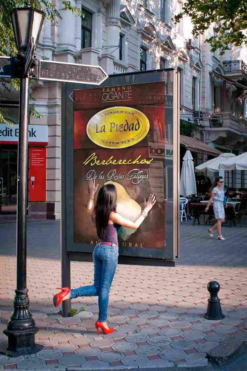 Una persona con una blusa morada, jeans y tacones rojos posa de forma divertida mientras toca una gran valla publicitaria de un restaurante al aire libre.